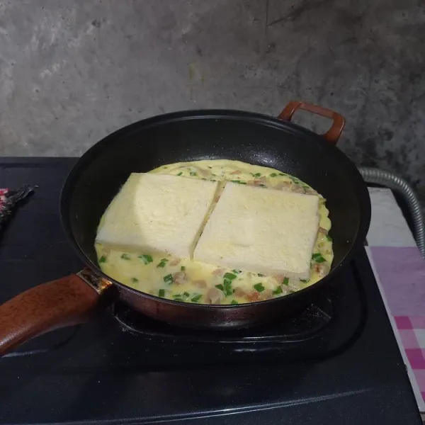 Nyalakan kompor dengan api sedang cenderung kecil. 
Tuang campuran isian pada pan yang sudah panas. 
Taruh roti tawar yang tidak diolesi margarin di atas telur goreng.