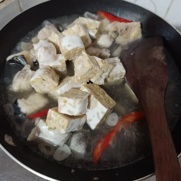 Masukkan tempe dan potongan ikan patin goreng, lalu tambahkan air dan biarkan mendidih.