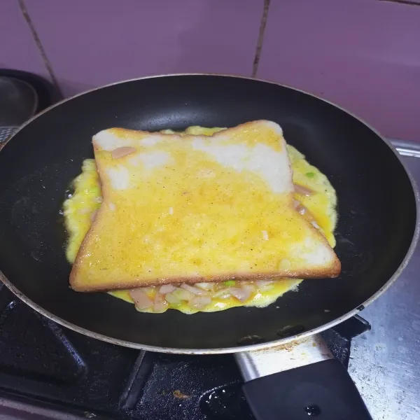 Letakkan roti tawar di atas telur sebentar, lalu balik roti tawar.