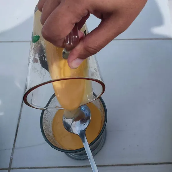 Tuang perlahan campuran kuning telur dan SKM diatas kopi dengan bantuan sendok.