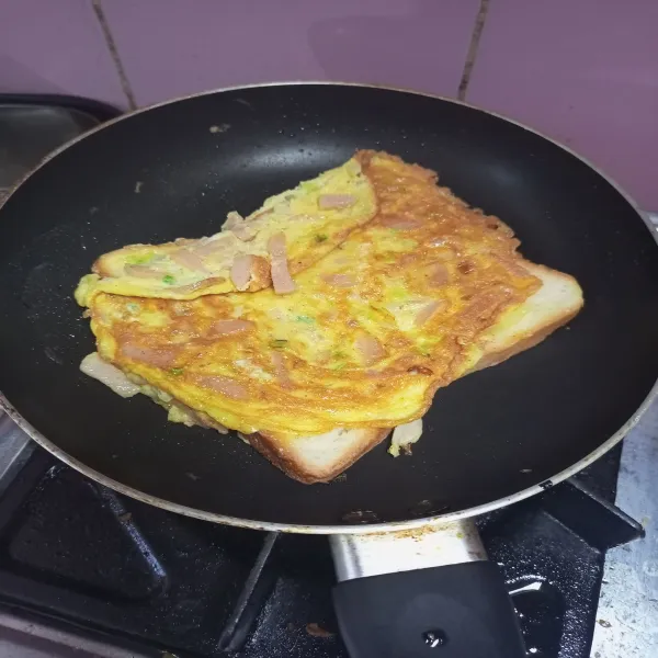 Setelah telur matang balik telur dan roti tawar. Biarkan sebentar supaya roti tawar berwarna kecokelatan. Lalu angkat dan letakkan di piring.