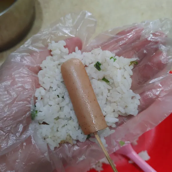 Setelah nasi hangat, ambil kurang lebih 2 sdm nasi, tambahkan sosis yang sudah diberi tusukan sate. Padatkan.