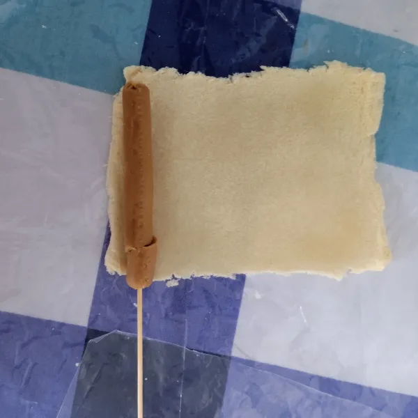 Tusuk sosis dengan tusuk sate, kemudian letakkan di atas roti tawar.