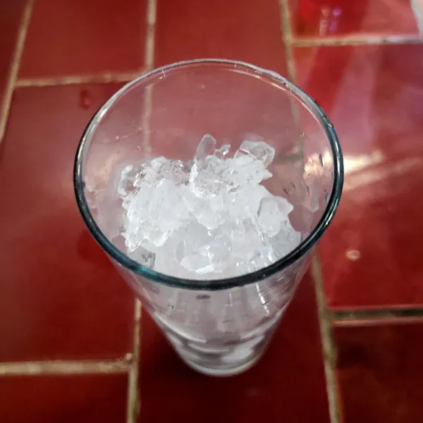 Siapkan gelas saji, lalu masukkan es batu hingga penuh.