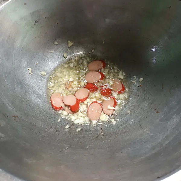 Panaskan minyak goreng, lalu tumis sosis dan bawang putih sampai harum.
