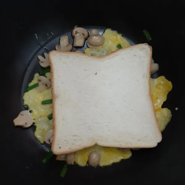 Letakkan roti tawar di atasnya saat telur masih ½ basah. Kemudian balik hingga posisi roti di bawah.