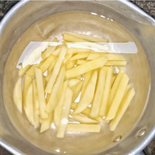 Kupas kentang, potong berbentuk stik panjang. Rendam dengan air, tambahkan garam, aduk rata. Diamkan minimal 30 menit. Bilas kentang berkali-kali hingga airnya jernih. Tiriskan.