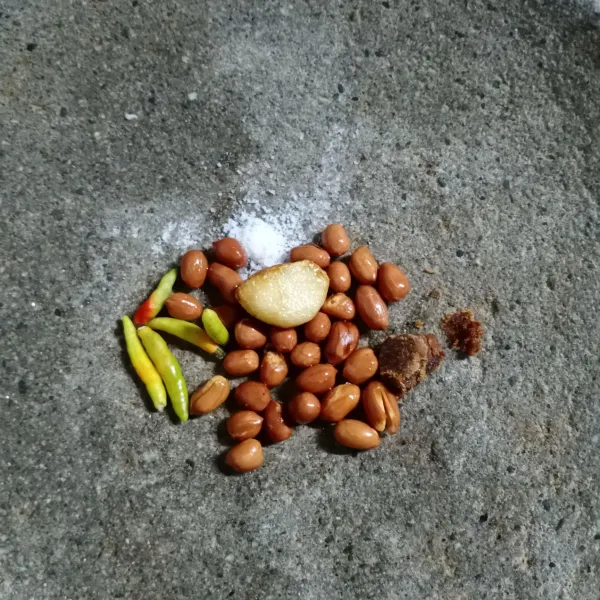 Haluskan bawang putih, kacang tanah, cabe rawit, gula merah dan garam. Beri sedikit air matang agar mudah mengulek.