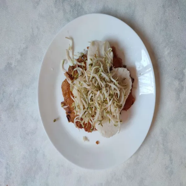 Tata telur dadar tahu di atas piring saji, lalu beri lontong dan taoge rebus.