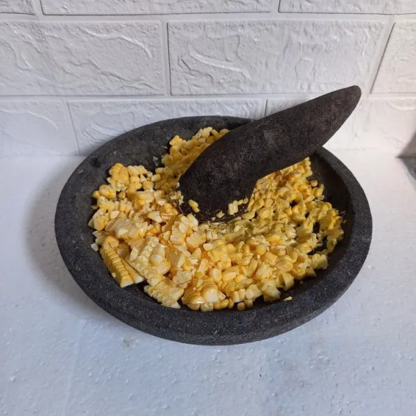 Pipil jagung dan ulek kasar. 
Pindahkan ke dalam wadah.