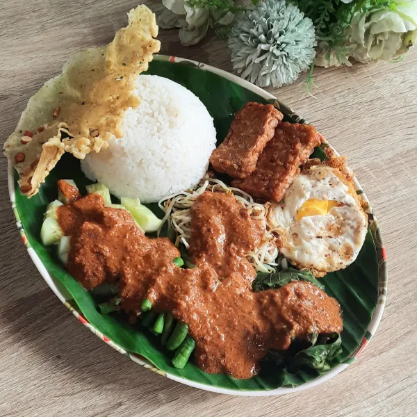 Tata nasi, sayur-sayur di atas piring, siram dengan bumbu dan beri rempeyek. 
Nasi pecel siap disajikan.