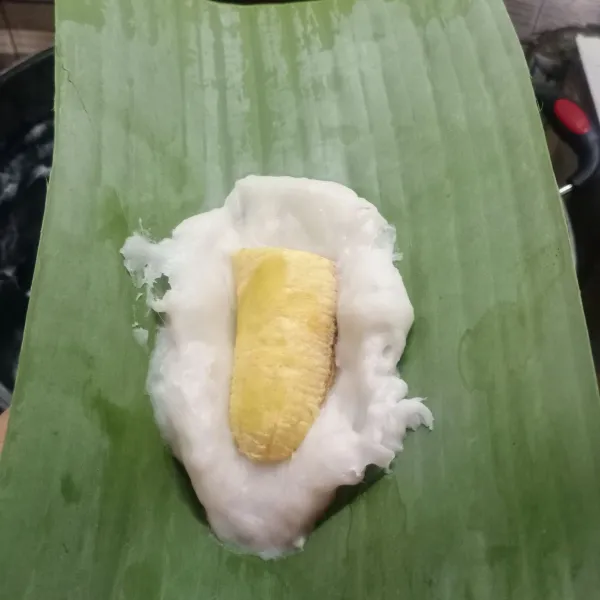 Siapkan selembar daun pisang. Beri adonan putih, letakkan sepotong pisang. Lalu tutup lagi dengan adonan putih.