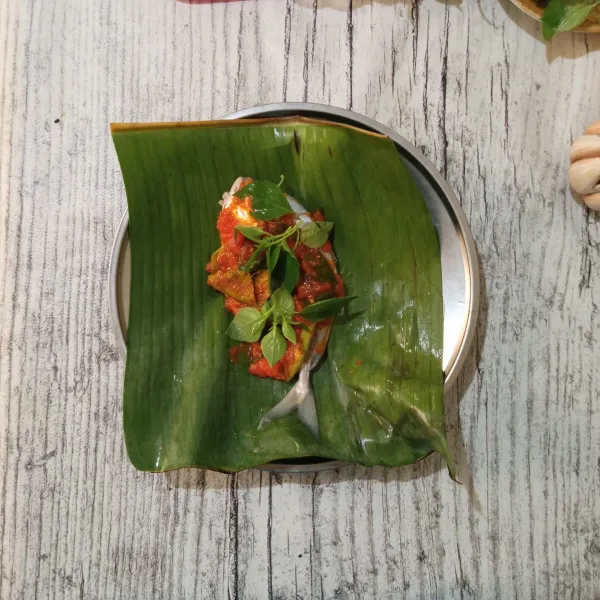 Letakkan ikan di atas daun pisang, baluri dengan bumbu tumis, tambahkan daun kemangi.