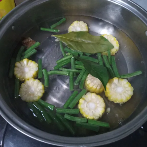 Didihkan air lalu masukkan jagung manis, kacang panjang, daun salam, dan lengkuas. Masak hingga setengah matang.