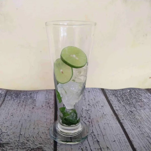 Masukkan es batu dan irisan jeruk nipis ke dalam gelas.