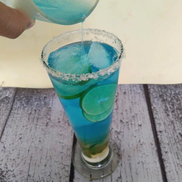 Tuangkan air soda berwarna biru ke dalam gelas sampai penuh.
Aduk sebentar lalu sajikan.