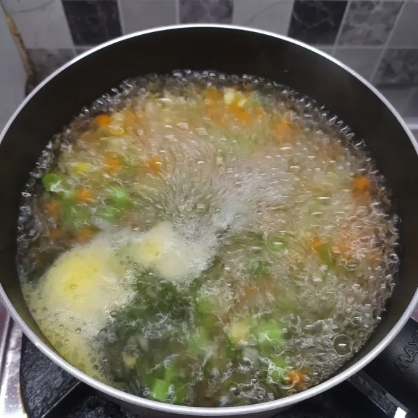 Rebus air kaldu sampai mendidih, masukkan wortel, jagung, buncis, daun bawang dan bombay. Masak sampai mendidih dan sayur ½ matang.