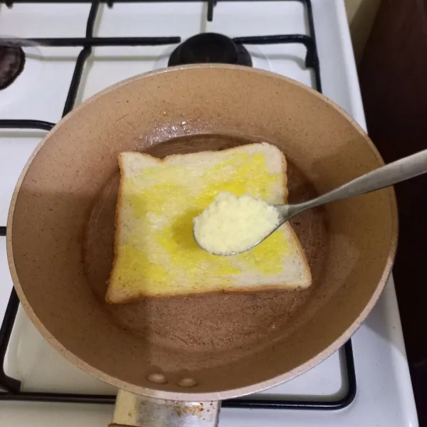 Beri keju parmesan pada permukaan roti, ratakan dan balikan roti hingga di kedua sisi berubah warna.