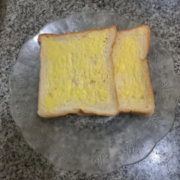 Olesi roti dengan margarin di satu bagian roti saja.