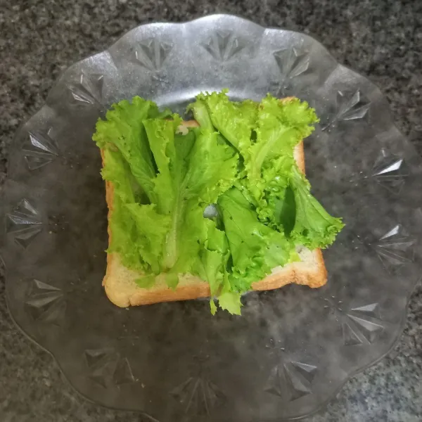 Tata roti dengan bagian yang dipanggang di bawah, tambahkan lembaran daun selada.