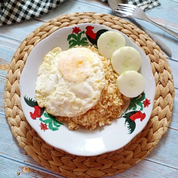 Sajikan nasi goreng dengan telur ceplok dan timun.