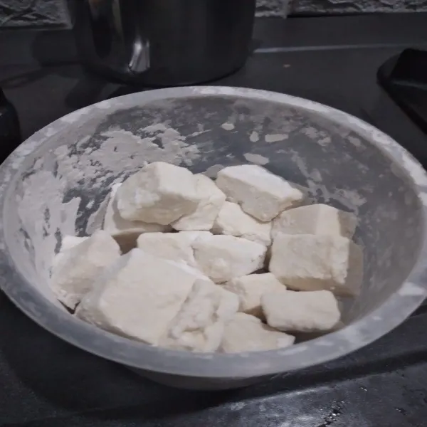 Angkat tahu dari pelapis basah, balurkan ke dalam wadah berisi tepung kering, dikocok-kocok supaya semua tahu terbalur tepung dengan merata.
