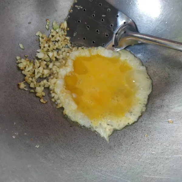 Sisihkan bawang putih di pinggiran wajan, lalu masukkan telur goreng dan orak-arik hingga matang.