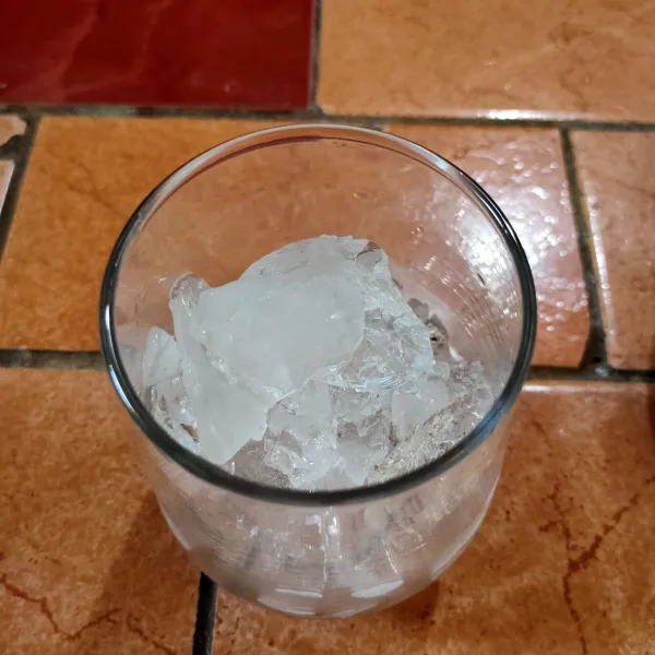 Siapkan gelas saji dan masukkan secukupnya es batu ke dalam gelas.
