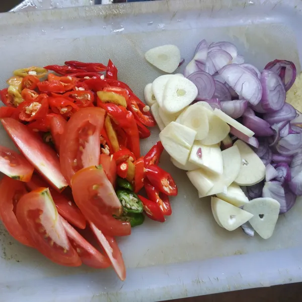 Potong-potong tomat, iris tipis bawang merah, bawang putih, dan iris serong cabai rawit dan cabai keriting.