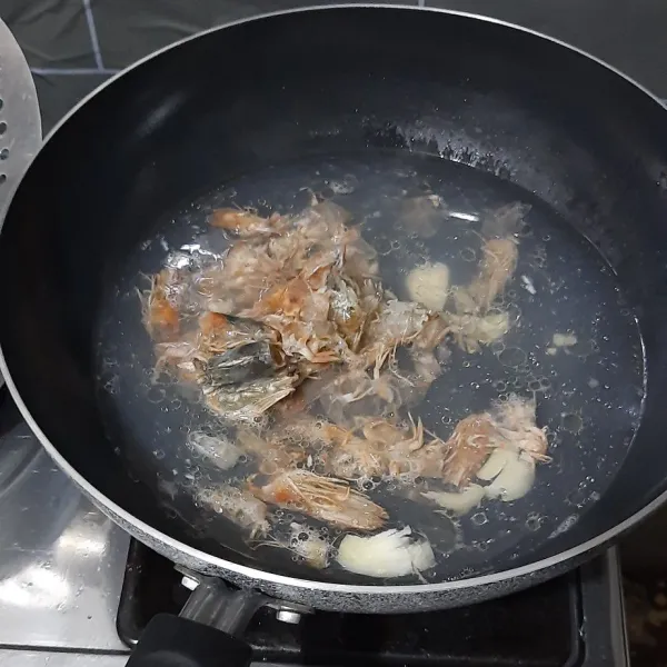 Panaskan minyak secukupnya, lalu tumis bawang putih hingga wangi. Kemudian tambahkan air dan masak hingga mendidih, lalu masukkan kepala udang.