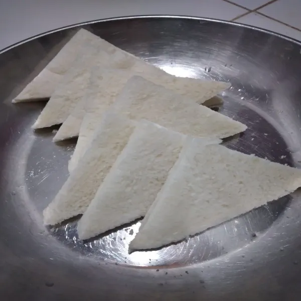 Potong lembaran roti tawar secara diagonal jadi berbentuk segitiga.