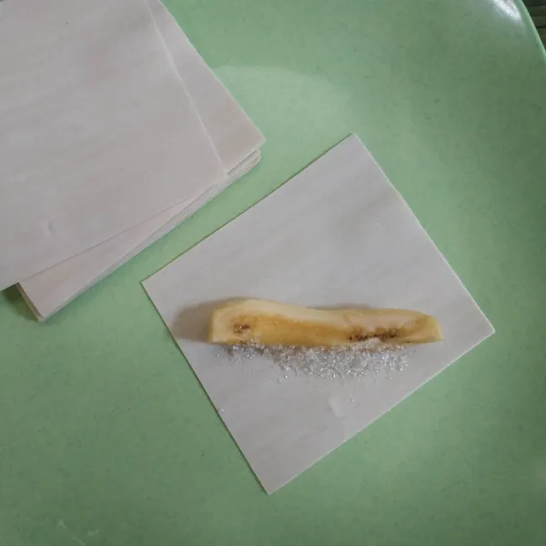 Ambil 1 lembar kulit pangsit, lalu tambahkan 1 potong pisang dan gula pasir secukupnya. Olesi bagian tepinya dengan bahan perekat, kemudian lipat seperti amplop dan gulung.