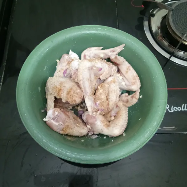 Masukkan sayap ayam ke dalam baskom, lalu tambahkan bawang merah, bawang putih, ketumbar bubuk, dan garam. Kemudian aduk rata dan diamkan sesaat.