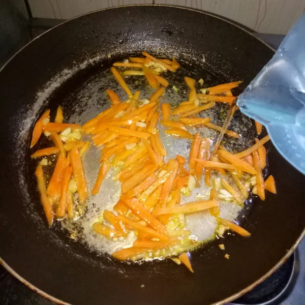 Siapkan pan dan panaskan minyak. Tumis bawang putih sampai harum, masukkan wortel dan air. Masak sampai air setengah surut dan wortel setengah matang.