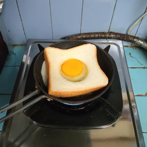 Bakar roti di atas teflon, lalu tuang satu butir telur ke dalam bagian tengah roti.