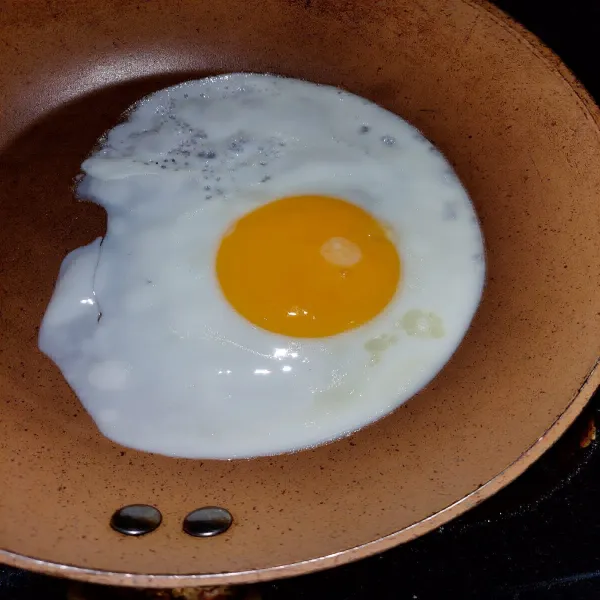 Panaskan wajan, lalu beri sedikit minyak goreng atau mentega. Buat telur sunny side atau telur ceplok setengah matang.
