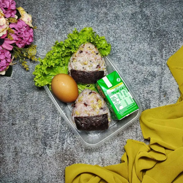Tata di atas lunch box, lengkapi dengan telur rebus dan susu cair. Onigiri Multigrain siap disajikan sebagai menu bekal anak.