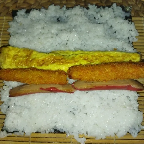 Tata 1 lembar nori di atas sushi matt, lalu tata nasi di atasnya, ratakan sambil ditekan, lalu tata telur gulung, sosis dan nugget.