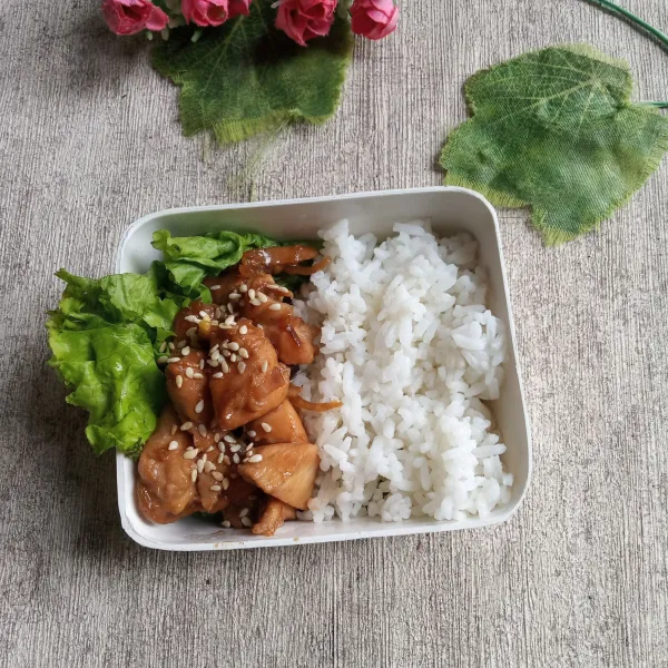 Tata dalam wadah bekal, selada, nasi putih hangat, tumisan ayam teriyaki dan taburi dengan wijen sangrai.