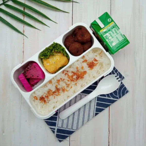 Tata nasi di dalam lunch box, beri taburan bawang goreng, masukkan bakso bakar, lengkapi dengan buah naga dan tahu goreng.