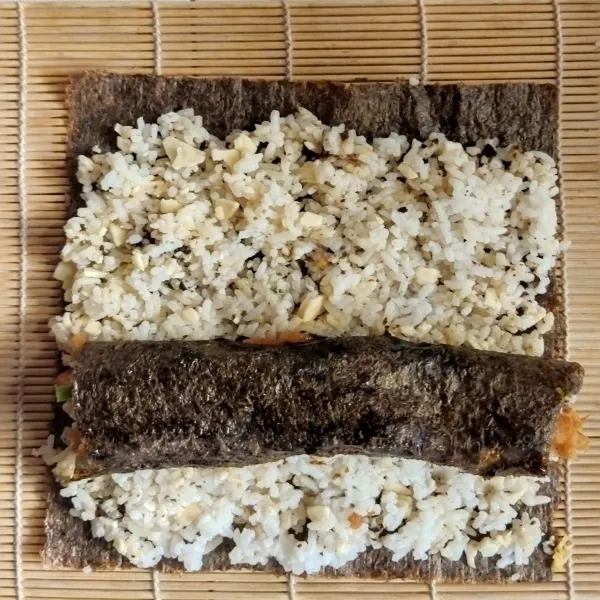 Siapkan 1 lembar nori, tambahkan di atasnya nasi jepang. Pipihkan nasi di atas nori hingga benar-benar tipis. Tambahkan gulungan ayam.