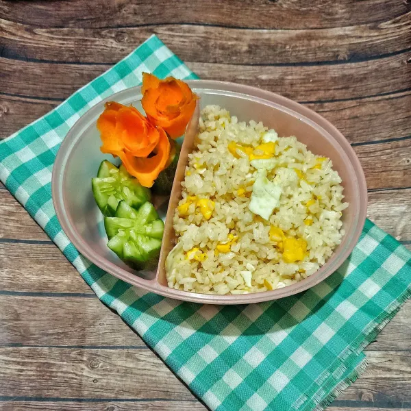 Masukkan nasi goreng ke dalam lunch box untuk bekal anak. Lalu taruh mentimun dan buat wortel berbentuk bunga. Siap dihidangkan.