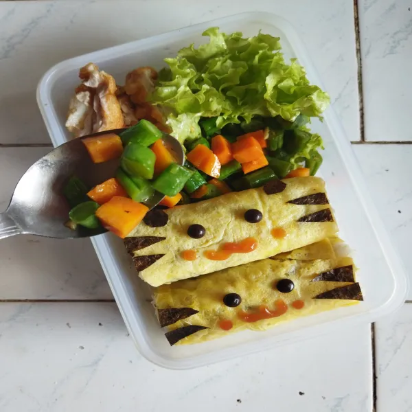 Bentuk mata dari nori lembaran dan aksesoris bento lainnya. Setelah itu, buka nasi dari plastic wrap pembungkusnya, kemudian tata nasi di atas kotak bekal dan susun nori yang telah dibentuk di atasnya sesuai selera. Tambahkan ayam karage yang telah digoreng dan tumisan sayur disebelahnya.