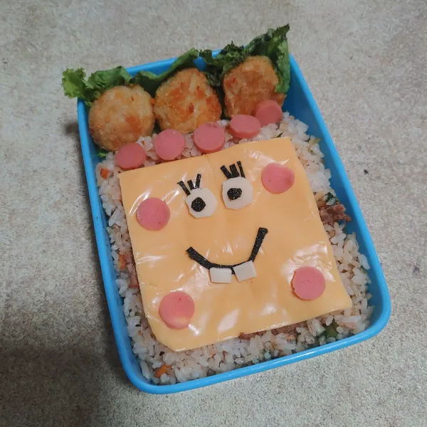 Ambil wadah bekal, masukan nasi goreng bolognese ratakan. Tambahkan nugget ikan dan hias dengan keju dan lain pelengkap lainnya hingga meyerupai spongebob. Bekal sikecil siap disajikan.