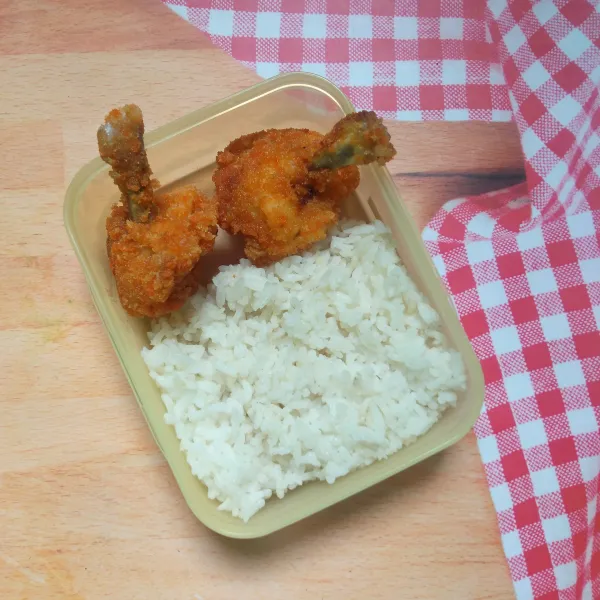 Tata nasi dan chicken drum stick ke dalam wadah makan, siap untuk bekal anak sekolah.