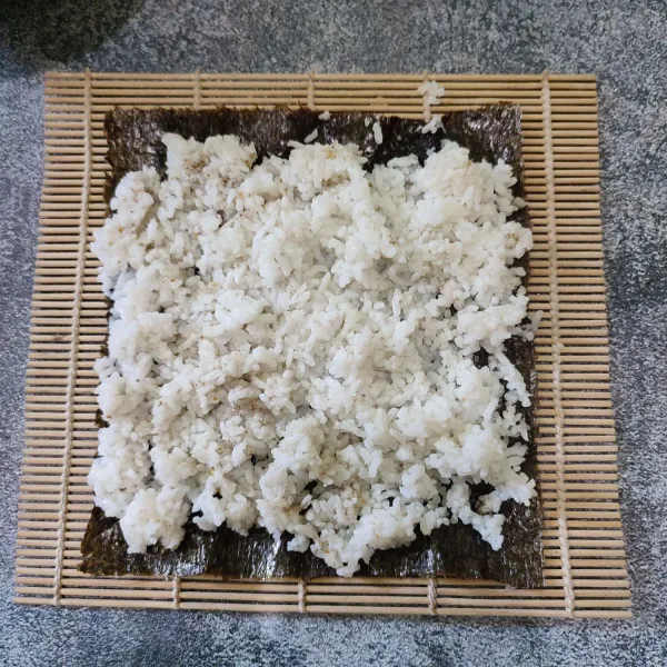Tata nori di atas sushi matt, kemudian beri nasi di atasnya.
