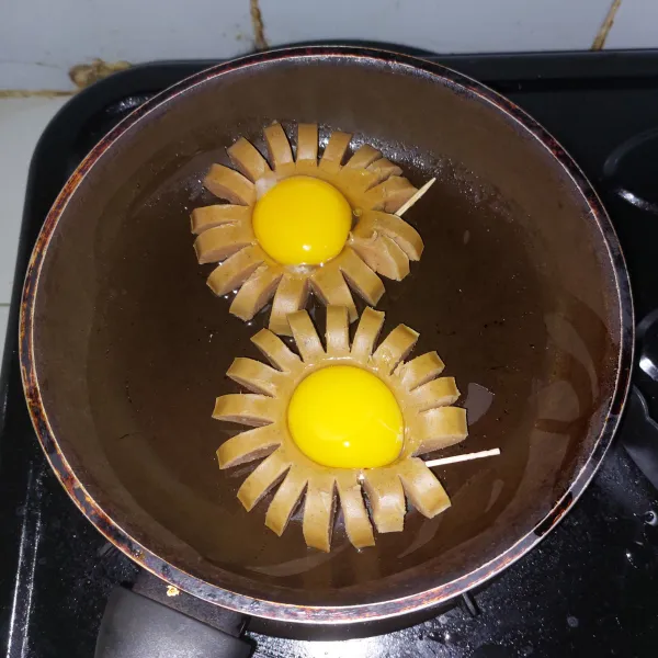 Pisahkan kuning telur. Letakkan kuning telur di tengah sosis. Gunakan sedikit minyak agar tidak lengket. Kalau ingin lebih cantik, tidak perlu dibalik. Tapi kalau untuk anak kecil lebih baik dibalik agar matang.