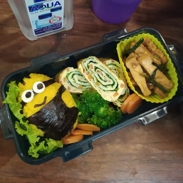 Kepal-kepal nasi kuning panas hingga membentuk bulat lonjong.
Beri hiasan dari nori dan keju menyerupai karakter Minion. Tata daun selada, telur gulung pokcoy, orek tempe tahu, wortel dan brokoli.