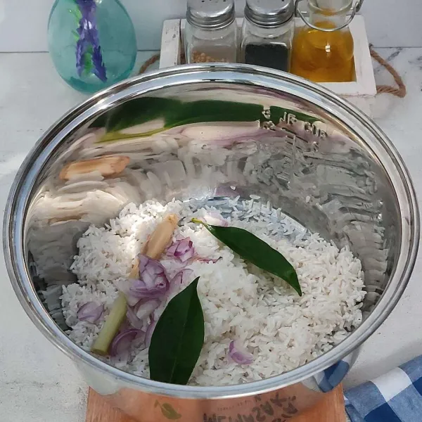 Masukkan beras yang sudah di cuci ke dalam rice cooker, kemudian tambahkan irisan bawang merah, serai geprek, garam, dan daun salam.