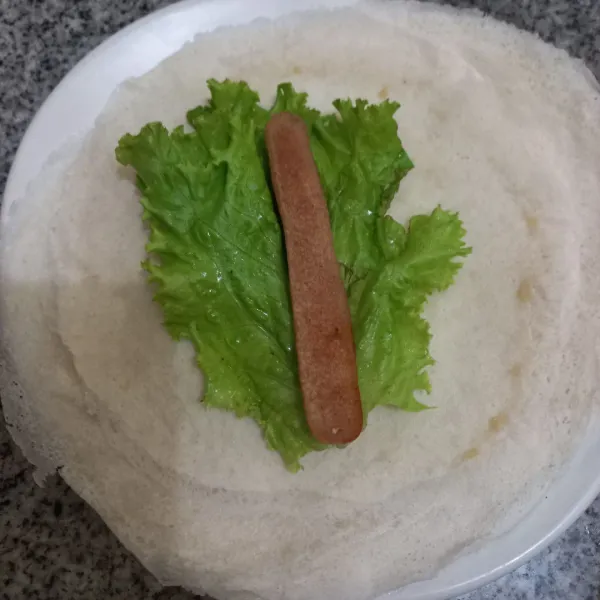 Tata daun selada dan sosis di atas kulit lumpia.